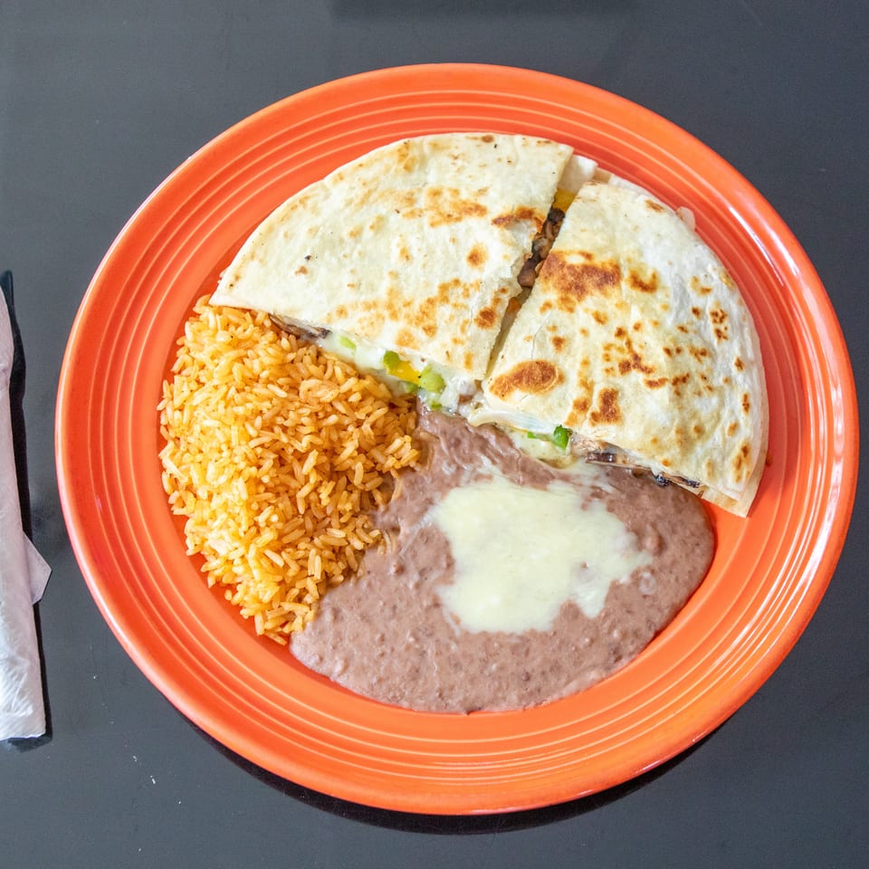 Mexican combination plate with grilled quesadillas, orange rice, and refried beans topped with melted cheese.