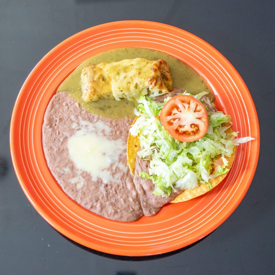Mexican combination plate with refried beans, a cheese-covered enchilada in green sauce, and a lettuce-topped tostada with tomato.