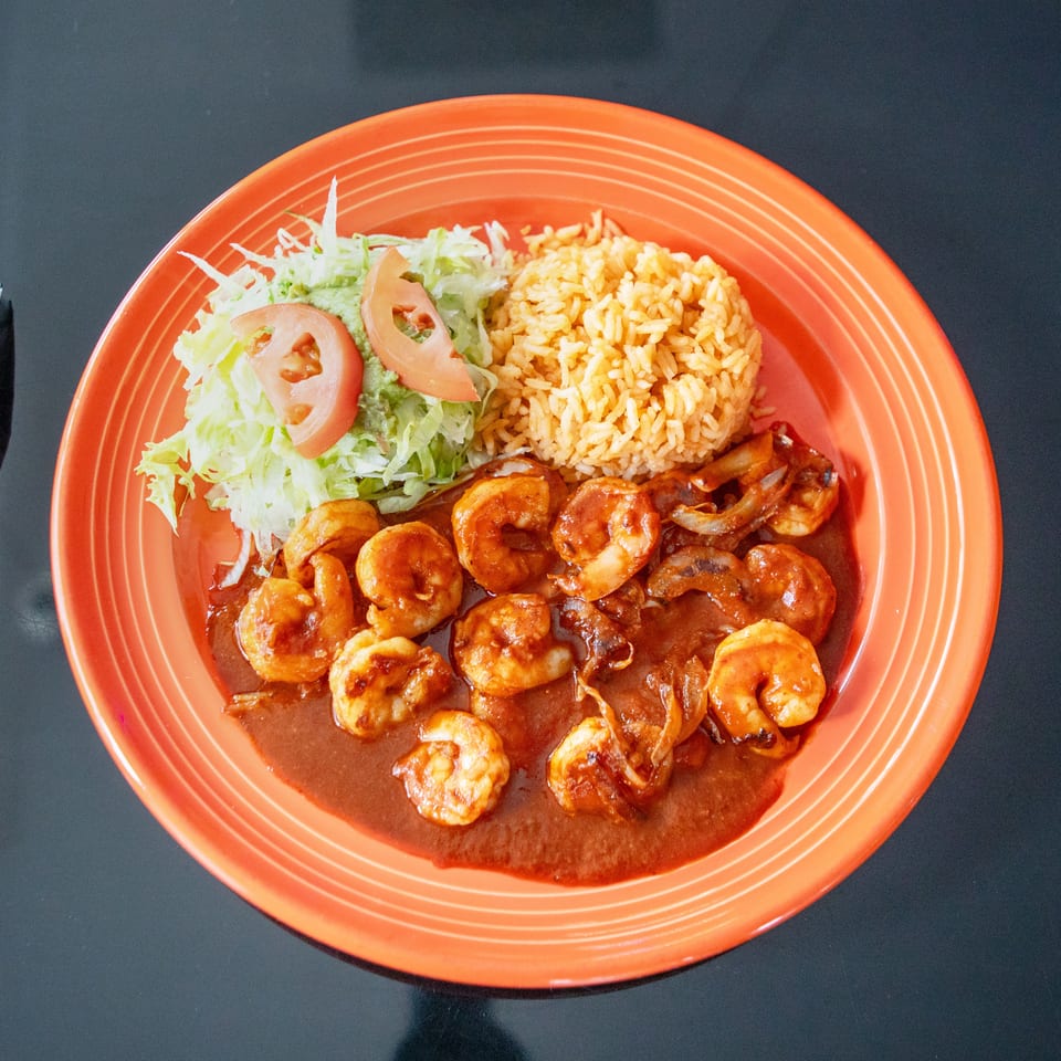 Orange plate of shrimp in red sauce with seasoned rice, lettuce, guacamole, and sliced tomatoes.